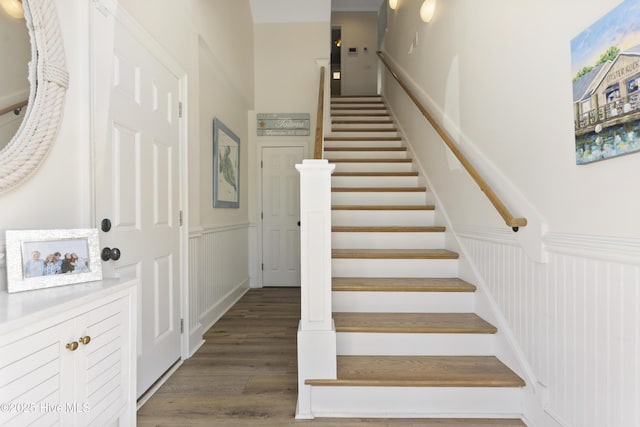 stairway with a wainscoted wall, a decorative wall, and wood finished floors