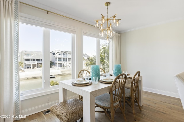 dining area featuring baseboards, visible vents, ornamental molding, an inviting chandelier, and light wood-style floors