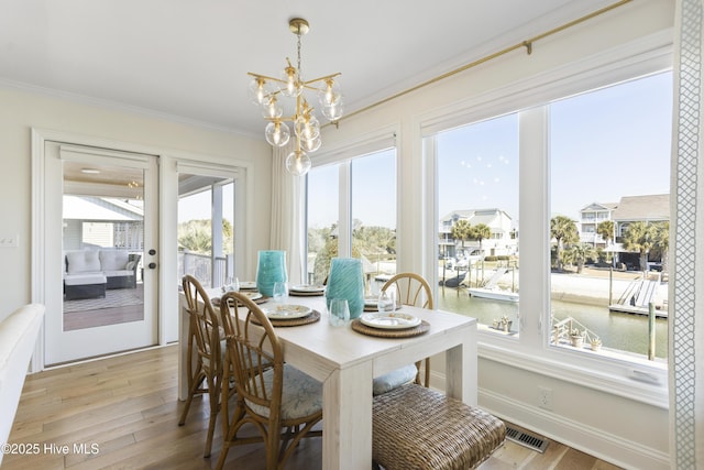 dining area with light wood-style floors, a healthy amount of sunlight, visible vents, and crown molding