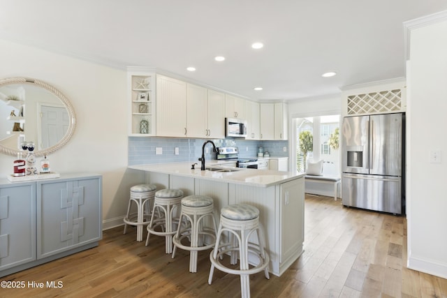 kitchen featuring stainless steel appliances, light countertops, light wood-style floors, open shelves, and a sink