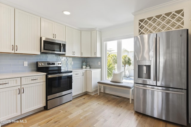 kitchen featuring light wood-type flooring, appliances with stainless steel finishes, light countertops, and decorative backsplash