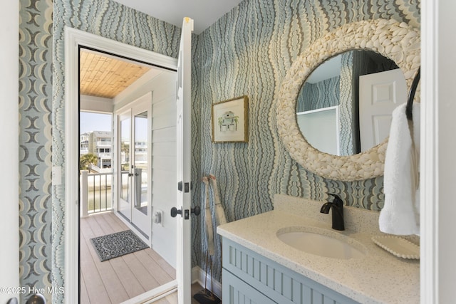 bathroom featuring wood finished floors, vanity, and wallpapered walls