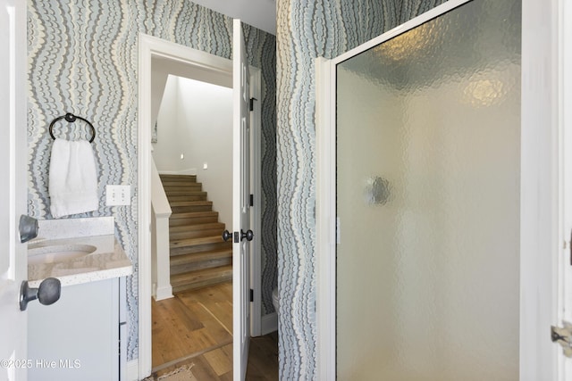 bathroom featuring a stall shower, wood finished floors, vanity, and wallpapered walls