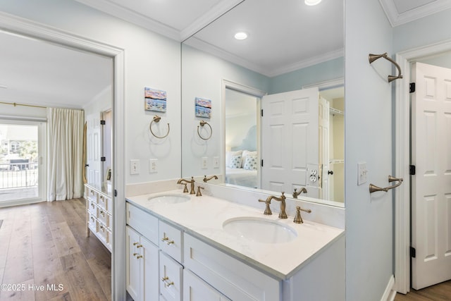 ensuite bathroom featuring crown molding, a sink, and wood finished floors