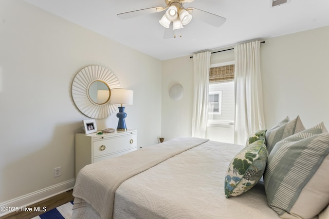 bedroom featuring a ceiling fan, visible vents, baseboards, and wood finished floors