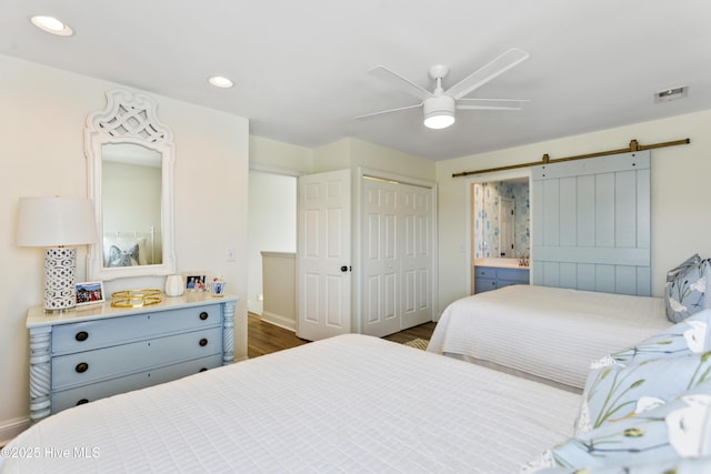 bedroom with a barn door, recessed lighting, visible vents, a closet, and dark wood finished floors