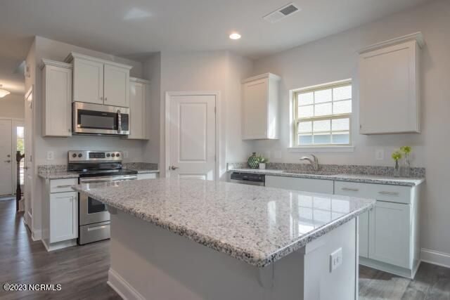 kitchen featuring a kitchen island, stainless steel appliances, dark wood-style flooring, and white cabinetry