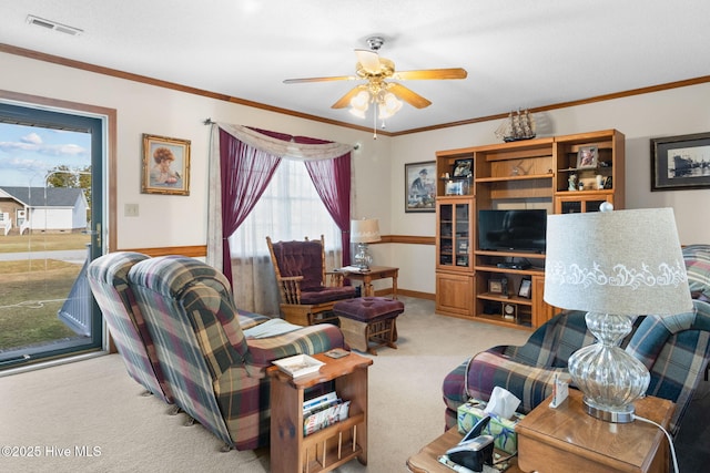 living area featuring baseboards, visible vents, a ceiling fan, light colored carpet, and crown molding