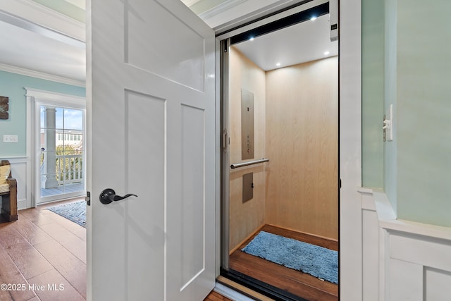 details featuring a wainscoted wall, ornamental molding, elevator, wood finished floors, and a decorative wall