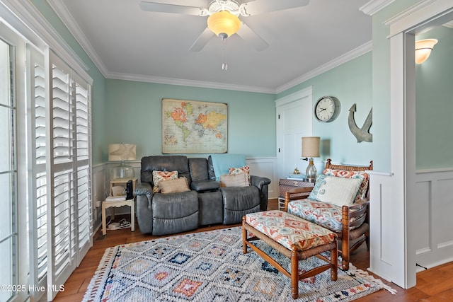 living area featuring a wainscoted wall, a ceiling fan, wood finished floors, and crown molding