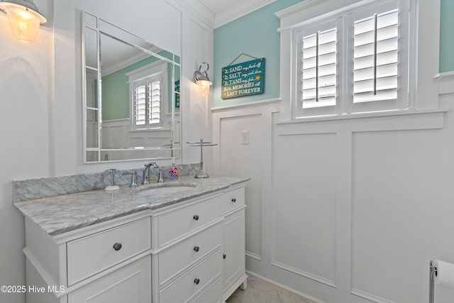 bathroom with a wainscoted wall, vanity, crown molding, and a decorative wall