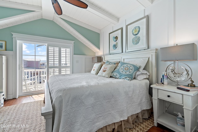 bedroom with wood finished floors, lofted ceiling with beams, wainscoting, access to outside, and a decorative wall