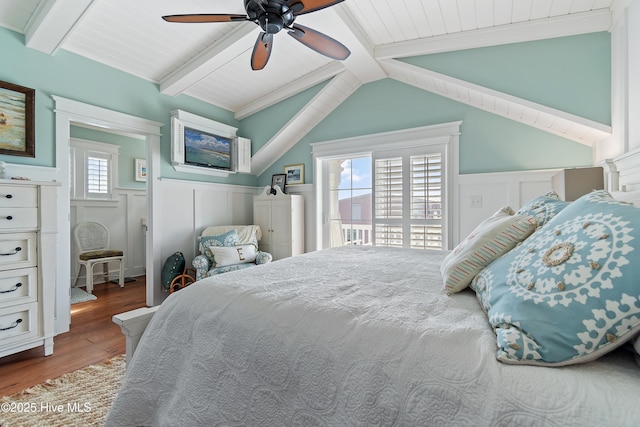 bedroom featuring a wainscoted wall, vaulted ceiling with beams, and wood finished floors