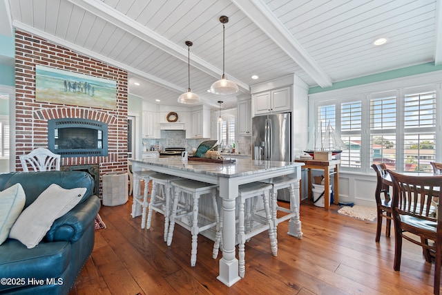 kitchen featuring lofted ceiling with beams, light stone counters, wood-type flooring, a fireplace, and decorative backsplash