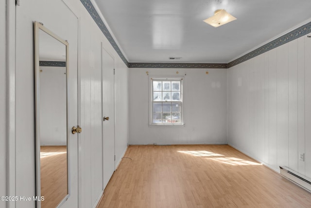 unfurnished bedroom with a baseboard heating unit, light wood-style flooring, visible vents, and crown molding