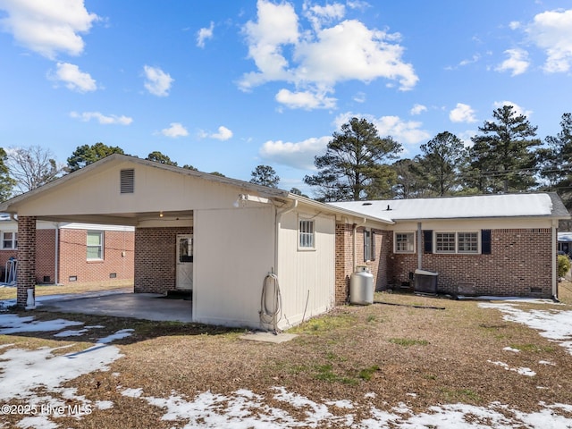 snow covered property with driveway, an attached carport, crawl space, cooling unit, and brick siding