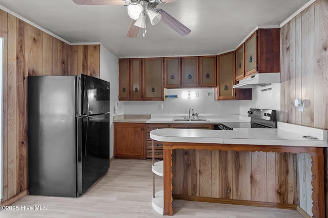 kitchen featuring under cabinet range hood, a peninsula, light countertops, brown cabinets, and black appliances