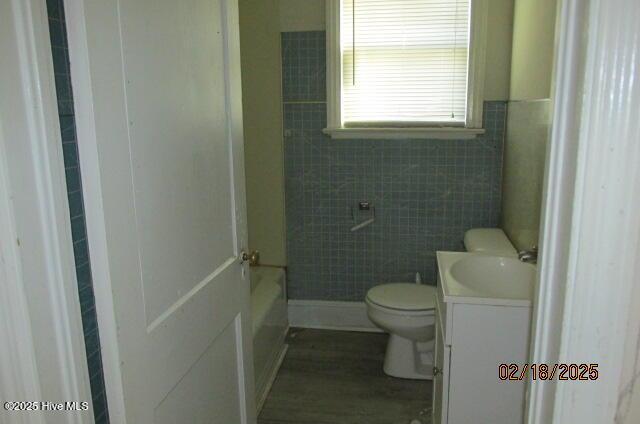 bathroom with a tub, vanity, toilet, and tile walls