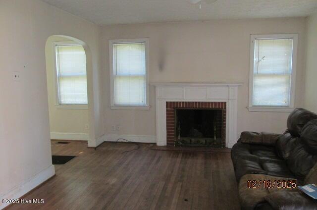 living room with a brick fireplace, baseboards, and dark wood finished floors