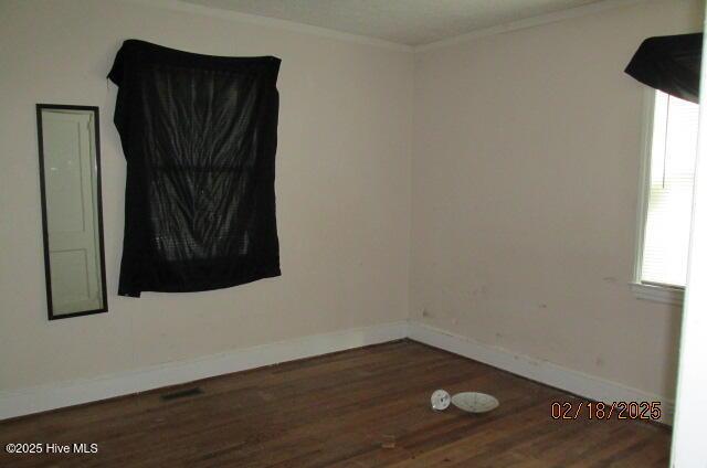 spare room featuring ornamental molding, a wealth of natural light, dark wood finished floors, and baseboards