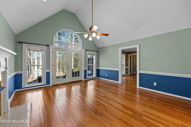 unfurnished living room featuring ceiling fan, wood-type flooring, french doors, high vaulted ceiling, and a high end fireplace