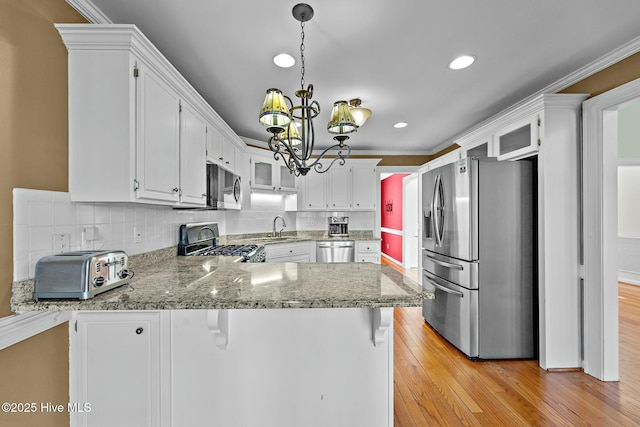 kitchen featuring stainless steel appliances, a peninsula, a sink, light wood-type flooring, and tasteful backsplash