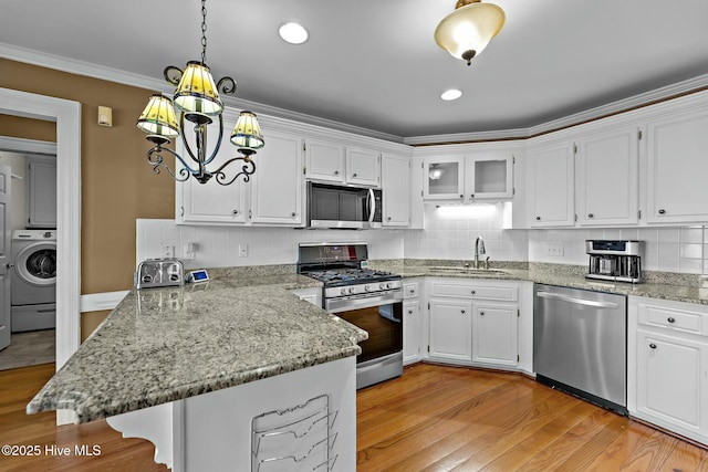 kitchen featuring washer / dryer, a peninsula, stainless steel appliances, white cabinetry, and a sink