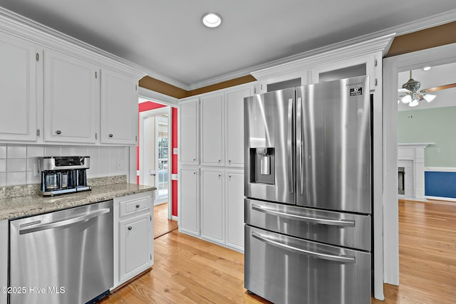 kitchen featuring stainless steel appliances, backsplash, light wood-style flooring, white cabinets, and light stone countertops