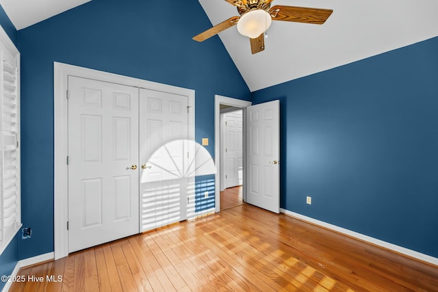 unfurnished bedroom featuring baseboards, hardwood / wood-style flooring, ceiling fan, high vaulted ceiling, and a closet