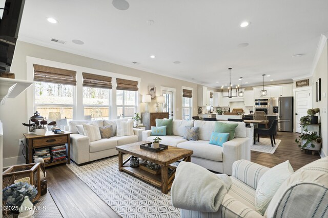 living area featuring ornamental molding, a glass covered fireplace, visible vents, and wood finished floors