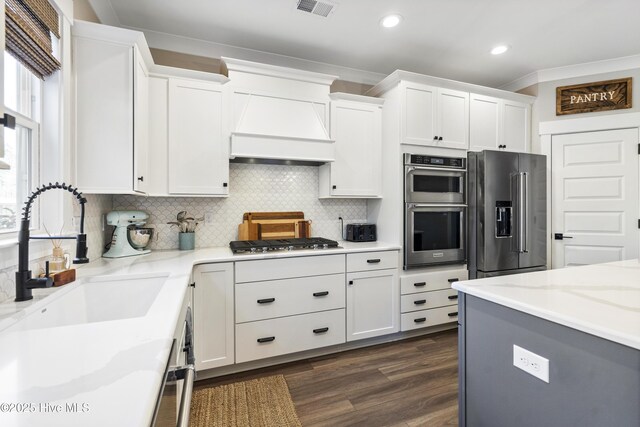 kitchen with stainless steel appliances, a sink, white cabinets, custom exhaust hood, and light stone countertops