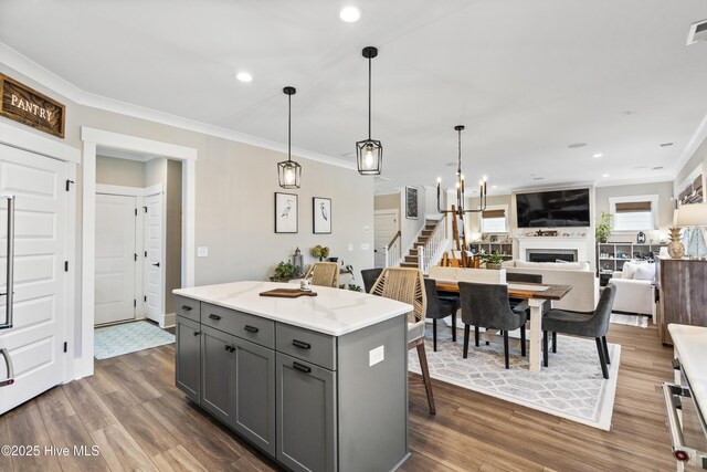 kitchen featuring dark wood-type flooring, gray cabinets, a center island, decorative light fixtures, and crown molding