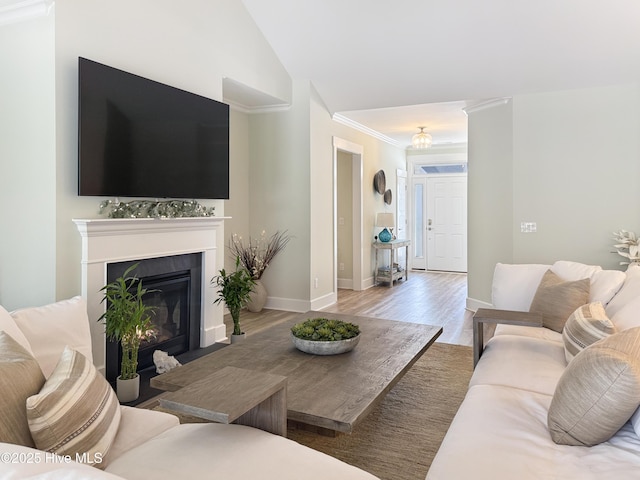 living room featuring vaulted ceiling, a fireplace with flush hearth, wood finished floors, and baseboards