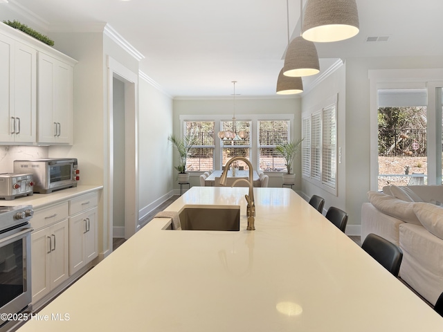 kitchen with stainless steel stove, visible vents, hanging light fixtures, ornamental molding, and a sink