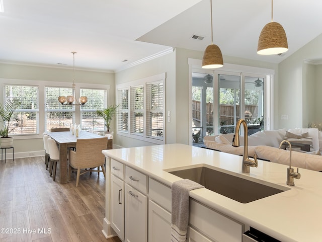 kitchen with visible vents, decorative light fixtures, crown molding, light wood-type flooring, and a sink