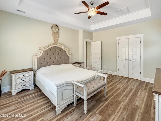 bedroom featuring a tray ceiling, visible vents, baseboards, and wood finished floors