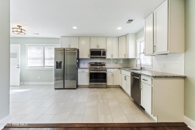 kitchen with visible vents, light stone counters, appliances with stainless steel finishes, a sink, and backsplash