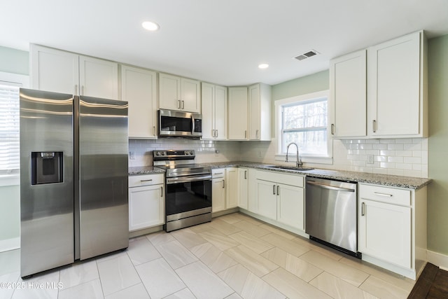 kitchen featuring stainless steel appliances, recessed lighting, tasteful backsplash, a sink, and dark stone countertops