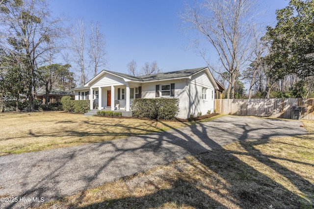 view of front facade featuring driveway, covered porch, fence, a front lawn, and brick siding