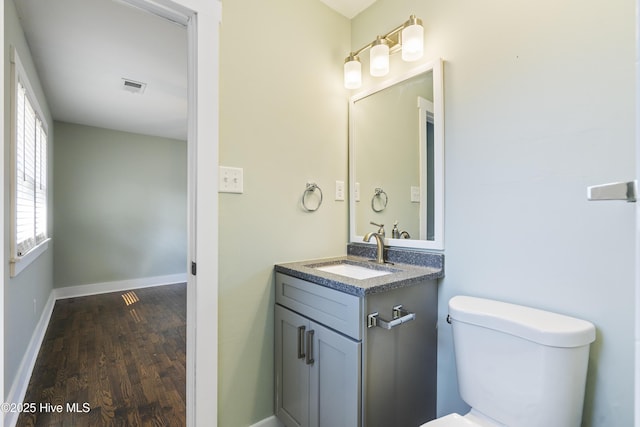 half bath with baseboards, visible vents, toilet, wood finished floors, and vanity