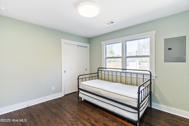 bedroom with wood finished floors, visible vents, baseboards, a closet, and electric panel