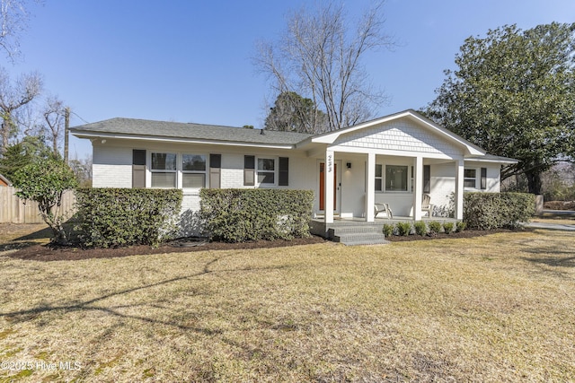 view of front of property featuring a front yard, covered porch, brick siding, and fence