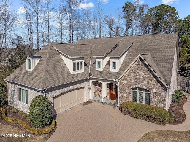 view of front of property featuring an attached garage, stone siding, decorative driveway, and roof with shingles