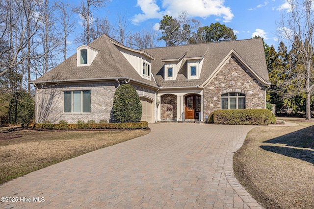 view of front of house with decorative driveway, brick siding, a shingled roof, a front yard, and stone siding