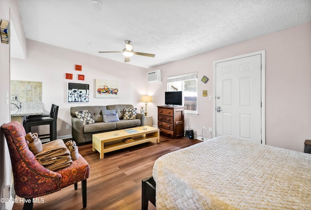 bedroom with a textured ceiling, ceiling fan, dark wood-type flooring, baseboards, and a wall mounted air conditioner