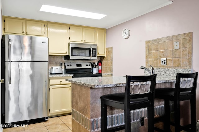 kitchen featuring light tile patterned floors, stainless steel appliances, a breakfast bar area, and backsplash