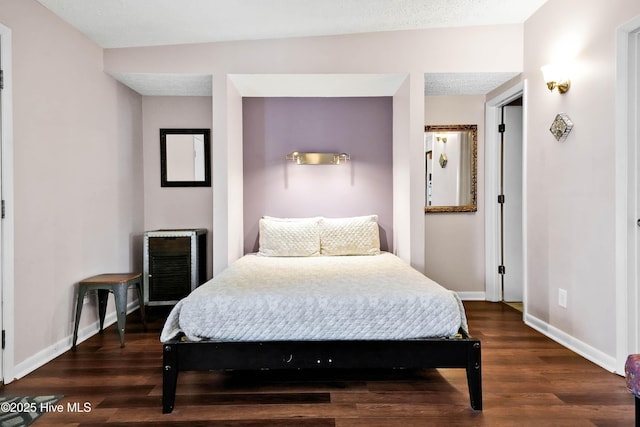 bedroom with a textured ceiling, dark wood-type flooring, and baseboards