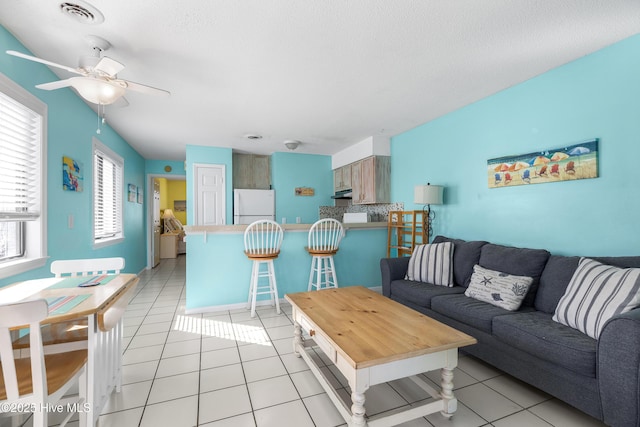 living area featuring a ceiling fan, visible vents, a textured ceiling, and light tile patterned floors