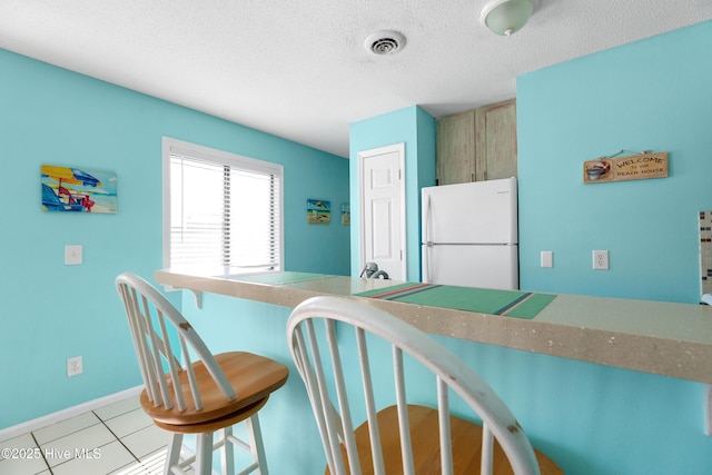 1618 Canal Dr Unit C-44, Carolina Beach, NC 28428 - kitchen featuring freestanding refrigerator, a breakfast bar, a textured ceiling, light tile patterned floors, and baseboards