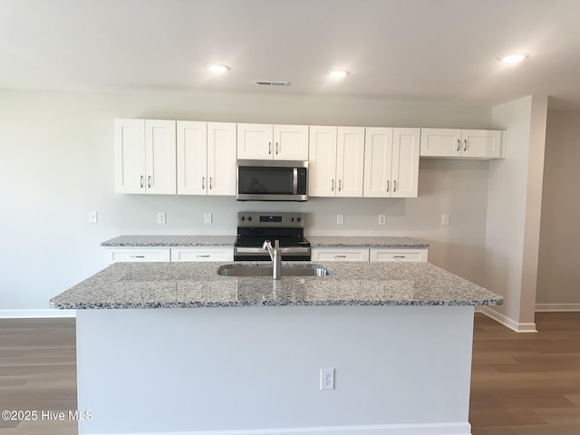 kitchen featuring visible vents, wood finished floors, light stone countertops, stainless steel appliances, and white cabinetry